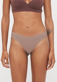 Bañador inferior de color marrón claro con un diseño en forma de V. Confeccionado en un material suave y elástico. Presenta una cobertura minimalista y un corte bajo.