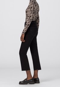 Svarta avkortade jeans med fransad fåll, matchade med en mönstrad långärmad topp och svarta loafers med en gyllene detalj.