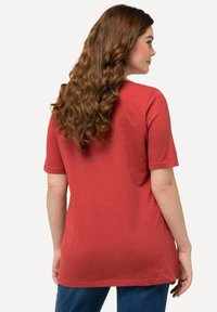 Camiseta de algodón roja con mangas cortas y cuello redondo, que presenta un corte relajado y una textura suave. La vista trasera muestra el cabello largo y ondulado.