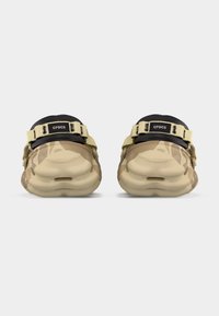 Ζευγάρι μπεζ και καμηλό καμουφλαρισμένα Crocs με μαύρα λουριά στο πίσω μέρος, εμφανισμένα από την πίσω όψη σε απλό λευκό φόντο.