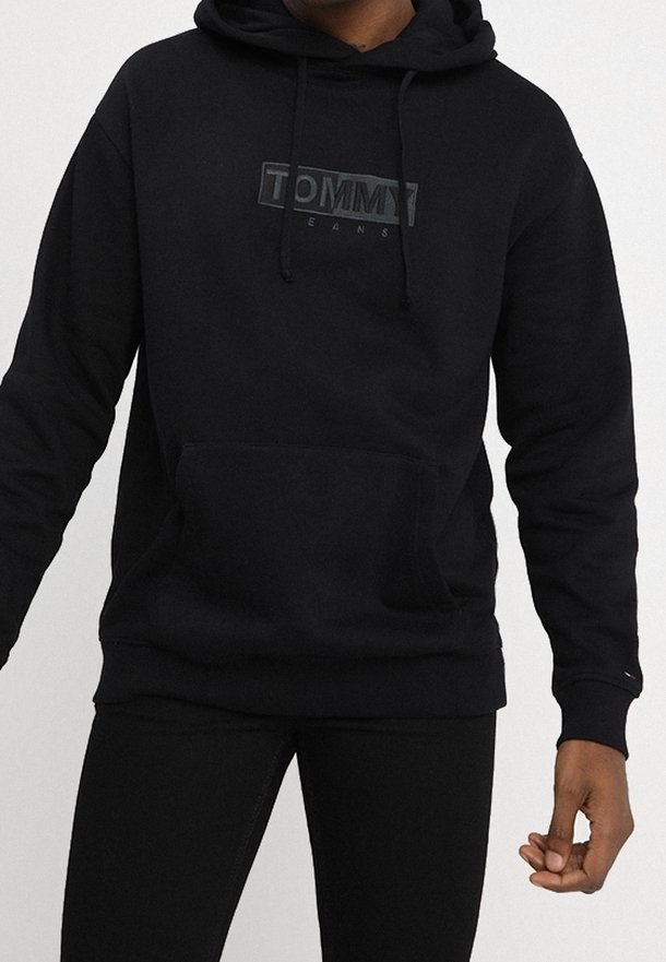 Černá bavlněná mikina s kapucí, která má přední kapsu a stahovací šňůrku. Na hrudi je matný nápis "TOMMY" a žebrované manžety.