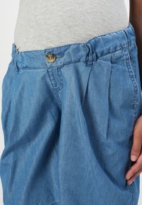 Light blue denim skirt with pleats at the front, a waistband with a button closure, and side pockets for added detail and functionality.