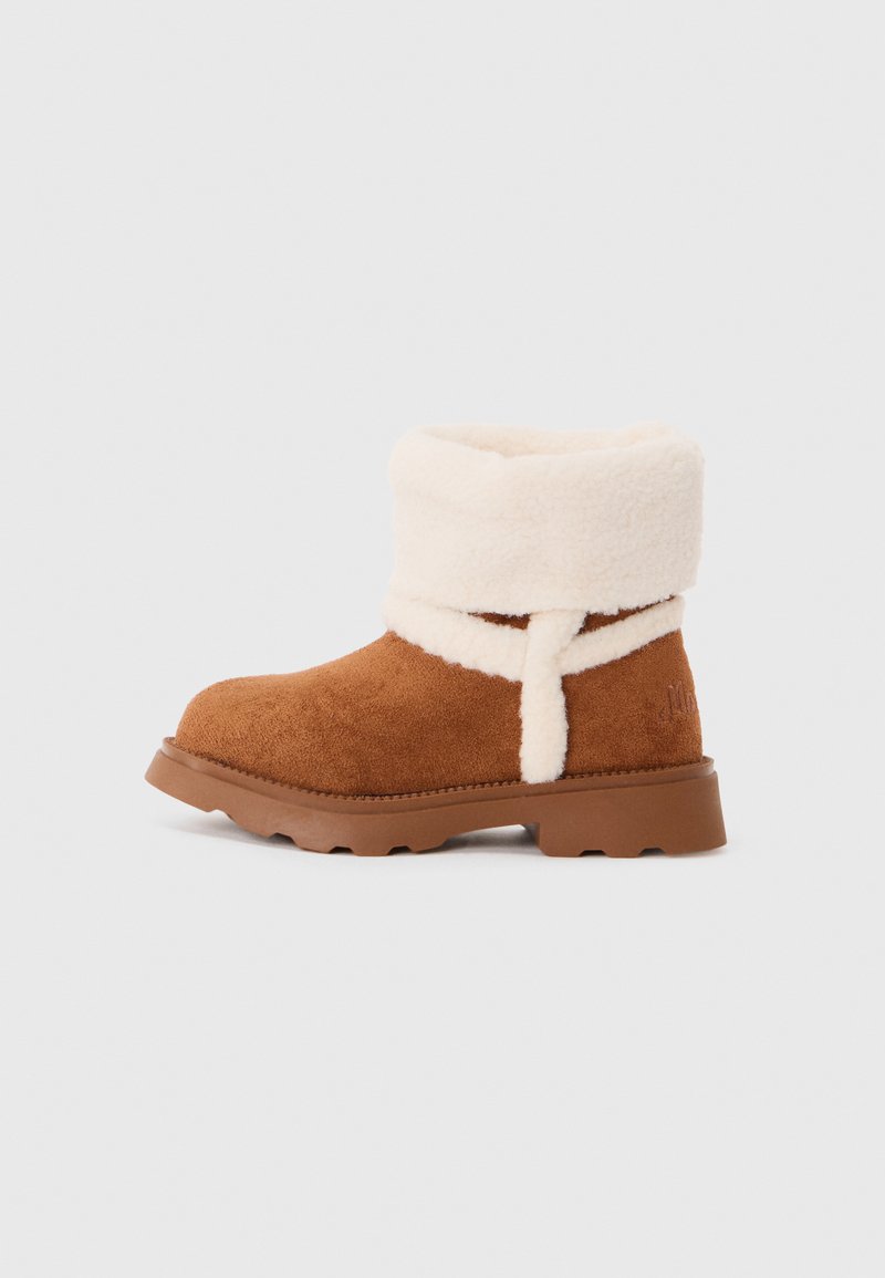 Bottine en suede marron avec un épais rebord et doublure en polaire beige, semelle plate en gomme et détail en polaire autour de la cheville.