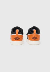 Black and orange sneakers with a white sole, featuring a pronounced heel tab, distinctive logo, and contrasting leather and textile materials.