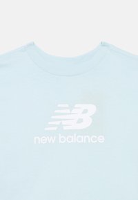 Lyseblå t-shirt med rund hals og et stort hvidt New Balance-logo samt brandnavn centreret på brystet.