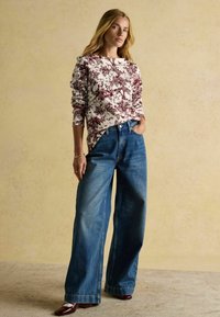 Biela košeľa s dlhými rukávmi a bordovými kvetinovými vzormi, doplnená o široké modré džíny. Oblečenie má voľný strih a hladkú textúru.