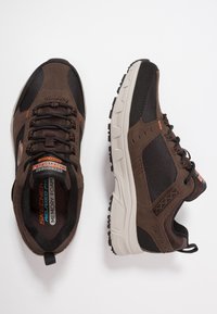 Brązowe buty sportowe z siateczkową i zamszową cholewką, czarnymi akcentami, wyściółką z pianki pamięciowej oraz teksturowaną gumową podeszwą.