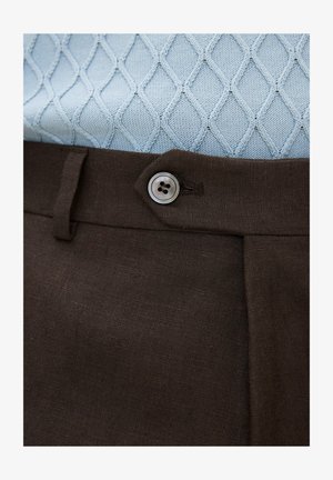 Jasnoniebieski sweter o fakturze dzianiny, włożony do ciemnobrązowych spodni zapinanych na jeden czterdziurkowy guzik.