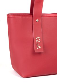 Rode leren tote bag met een gestructureerde vorm, gladde textuur en een zichtbaar gouden logo accent op de strap.