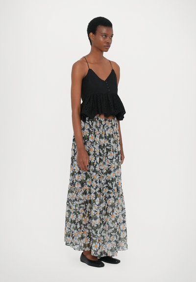 Schwarzes Peplum-Top mit Spitze und Knöpfen, kombiniert mit einem bodenlangen Rock mit Blumenmuster, der Gänseblümchen auf dunklem Hintergrund zeigt. Schwarze Ballerinas.