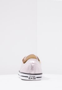 Světle růžové plátěné tenisky s nízkým střihem, černou gumovou podrážkou a bílými pruhy. Mají texturovanou látku a prošívání na patě.