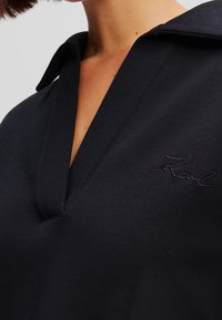 Camisa polo negra con cuello con muesca y un discreto logotipo bordado. Tejido suave con un diseño simple y limpio.