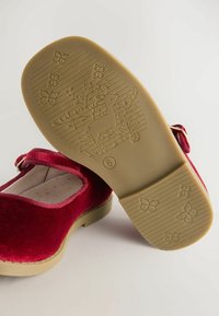 Rode fluwelen kinderschoenen met een ronde neus, platte zool en verstelbare band; zool heeft een hert- en bloemmotief.