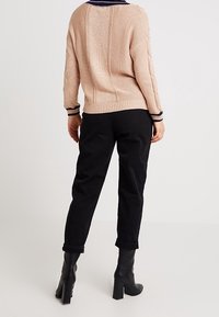 Maglione lavorato a maglia rosa chiaro con motivo testurizzato e colletto blu navy, abbinato a pantaloni neri tapered e stivali neri con tacco al ginocchio.
