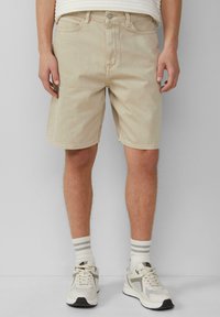 Beige denim shorts met een rechte pasvorm, voorzakken en een ritssluiting. Gecombineerd met witte sneakers en gestreepte crew-sokken.