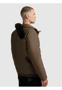 Brązowa ocieplana kurtka z teksturowanym czarnym sztucznym futrzanym kołnierzem, zapinana z przodu na zamek błyskawiczny, o dopasowanym kroju, widziana z boku.