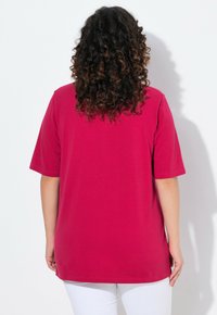 T-shirt magenta a maniche corte con vestibilità rilassata, realizzato in morbido cotone e orlo dritto. La vista posteriore mostra i dettagli della cucitura sulla spalla.