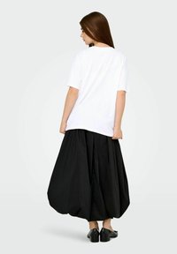 White oversized t-shirt with short sleeves paired with a voluminous black skirt. The skirt features a smooth texture and a rounded shape.