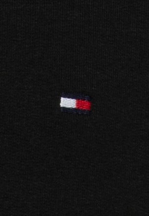 Małe prostokątne wyhaftowane logo z białymi, czerwonymi i ciemnoniebieskimi sekcjami na czarnym materiale.