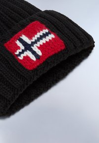 Gorro de punto negro con un parche rojo que presenta un diseño de cruz nórdica en blanco y azul. La tela tiene un aspecto texturizado y acogedor.