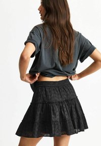 Svart lager-skirt gjord av lätt tyg med broderade prickar. Elastisk midja, utsvängd form och knälång design.