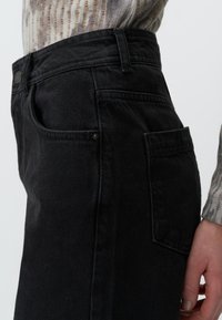 Jeans in denim neri con taglio dritto, tasche laterali e finitura testurizzata, dotati di passante per cintura e dettaglio con bottone in vita.