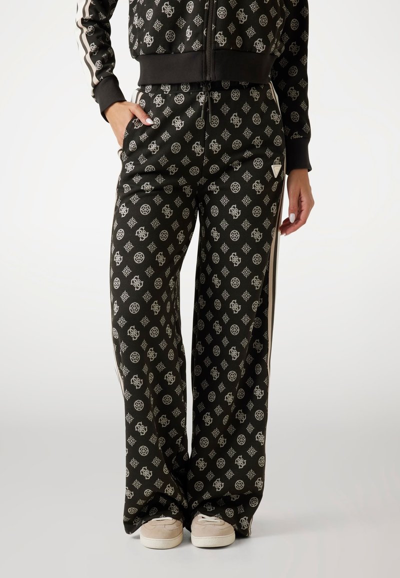 Sorte mønstrede træningsbukser med hvide geometriske designs, brede ben og sidelister, parret med lyse slip-on sko.