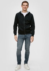 Felpa nera con zip e interno grigio, maniche lunghe, tasche a marsupio, abbinata a jeans slim-fit e sneakers bianche.