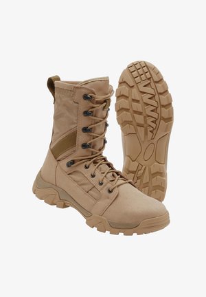 Barna taktikai bakancs boka magasságú fűzővel és masszív gumitalppal, az egyik bakancs áll, a másik a talpmintát mutatja.