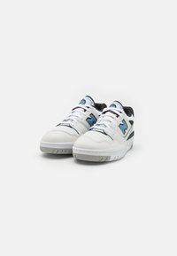 Valge ja sinine New Balance jooksujalatsite paar, millel on paelad, must sisemine vooder ja hall tald, lihtsal valgel taustal.