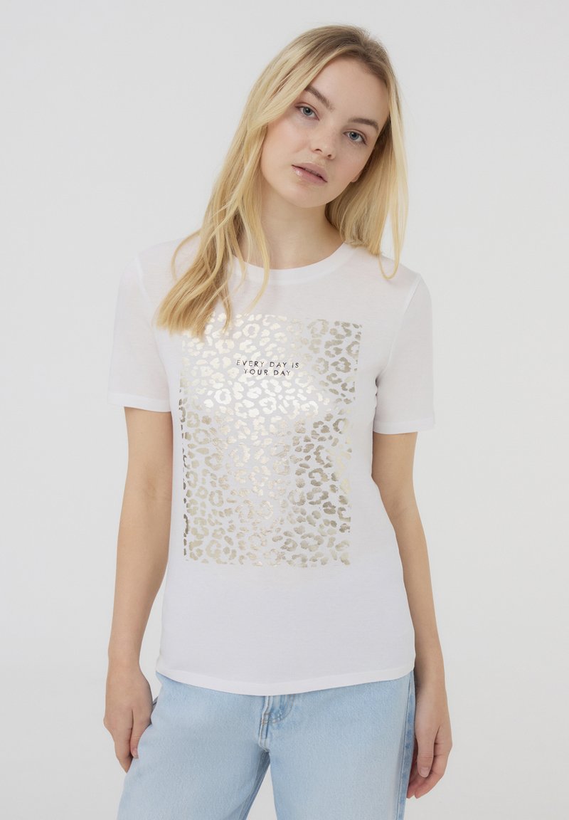 T-shirt bianco a maniche corte con un design in stampa leopardata dorata e la scritta "OGNI GIORNO È IL TUO GIORNO" al centro.