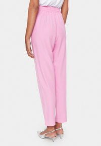 Rosa Hose mit elastischem Bund, geradem Beinansatz und glatter Textur. Kombiniert mit silbernen Slingback-Absätzen.
