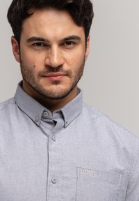 Jasnoszara koszula zapinana na guziki z kołnierzykiem, kieszonką na piersi z haftem "LEE COOPER" oraz gładkim, teksturowanym materiałem.