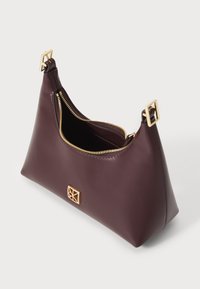 Geantă din piele sintetică burgundy, cu un fermoar auriu, având o formă triunghiulară structurată și un logo embossat pe față. Curea ajustabilă.
