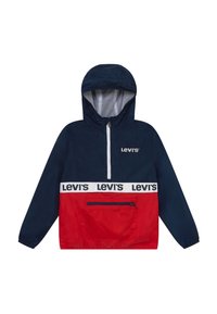 Röd och marinblå vindjacka med huva, halvdragkedja framtill, vit randad logotyp vid midjan, samt en framfick med dragkedja. Slätt, lätt material.