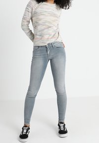 Helle graue Skinny Jeans mit mittlerer Taille und sanften Ausbleichungen. Kombiniert mit einem mehrfarbigen Strickpullover und schwarzen Sneakers.