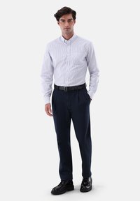 Weiß gestreiftes Hemd mit Knöpfen, marineblaue Anzughose, schwarzer Gürtel und schwarze Schuhe. Die Hose hat eine gerade Schnittform, das Hemd verfügt über einen Kragen und Knöpfe.