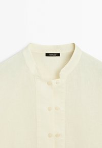 Crèmekleurig overhemd met opstaande kraag en drie paar kleine knopen aan de voorkant, met label Massimo Dutti, gemaakt in Marokko.