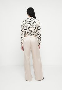 Fekete és bézs tigriscsíkos gombos ing bézs, széles szárú szatén nadrággal, sima textúrával és szabott szabással.