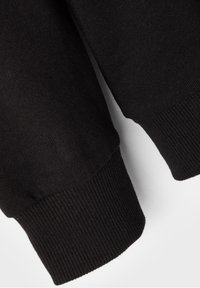 Puño de suéter negro de punto que muestra una textura acanalada, un acabado suave y bordes limpios. El material parece suave y flexible con un color uniforme.