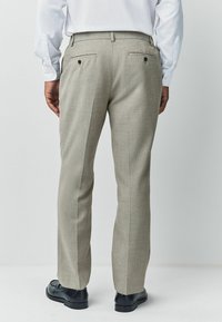 Light gray trousers with a checkered texture, flat back pockets, and black buttons, paired with black shoes. Rear view shown.