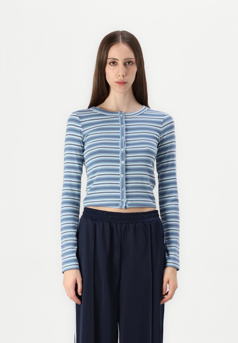 Camisola de mangas longas às riscas em tons de azul, com decote redondo e fechamento em botões, combinada com calças largas azul-marinho.