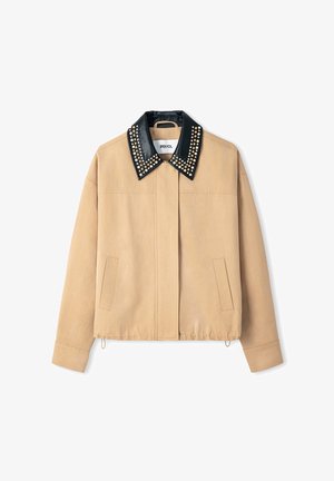 Giacca beige con colletto nero chiodato, dotata di chiusura a bottoni e tasche laterali. Tessuto liscio con un design dalla vestibilità rilassata.