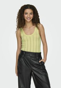 Limoengroene gebreide tanktop met verticale strepen, gecombineerd met hoge zwarte faux leren broek met grote knopen en zijzakken.