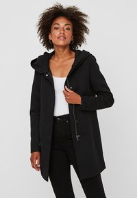 Cappotto nero con cappuccio realizzato in tessuto morbido, dotato di zip e bottoni a pressione, con una vestibilità comoda e tasche laterali.