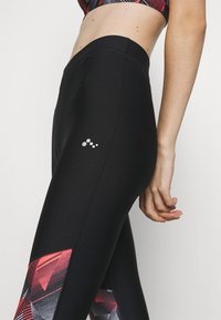 Leggings neri in tessuto liscio con un motivo geometrico rosso e nero e un piccolo logo bianco sulla coscia.