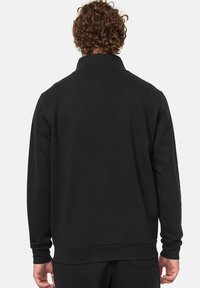 Sudadera negra con cuello alto, puños y dobladillo acanalados, tejido texturizado y un ajuste casual. Presenta un diseño liso en la parte posterior.