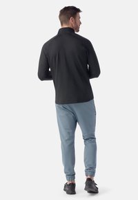 Schwarzes Langarmshirt mit Reißverschlusskragen, kombiniert mit hellblauen Jogginghosen mit elastischen Bündchen. Das Outfit beinhaltet schwarze Sportschuhe.