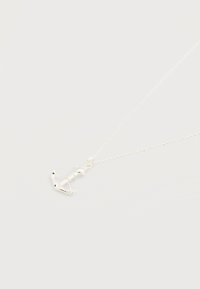 Ασημένιο κολιέ με ένα μικρό μενταγιόν σε σχήμα άγκυρας σε μια λεπτή αλυσίδα πάνω σε λευκό φόντο.