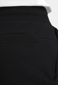 Pantaloni jogger neri con una texture liscia, dotati di una cintura a costine e dettagli sui taschini. Il design enfatizza il comfort e una vestibilità informale.